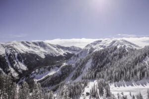A picture of two mountains. The one on the right is round and covered in snow with ski runs down it. The left is pointed at the top of long snowy slopes. The sky is bright blue.